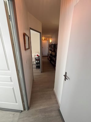 A hallway with a white door on the left, a white wall with a framed picture, and a wooden floor. - Small townhouse in a rural seaside setting (10-minute walk to shops and the beach) (Saint-Valery-en-Caux)
