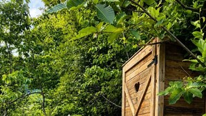 A wooden shed and a tent in a natural setting with trees and a dirt path.