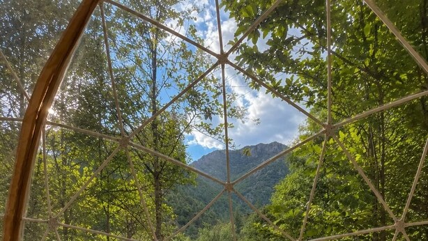 A room with a bed, pillows, and a view of a forest through a geometric window structure.