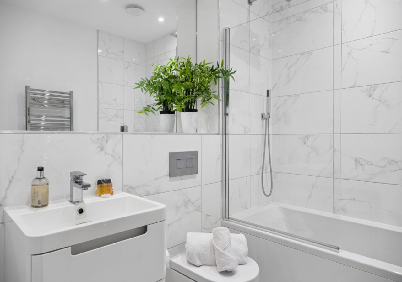 A modern bathroom with a white sink, a glass shower enclosure, and a potted plant.