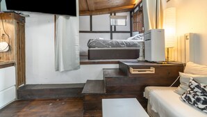 Habitación pequeña con cama, televisión, lámpara y escalera de madera.