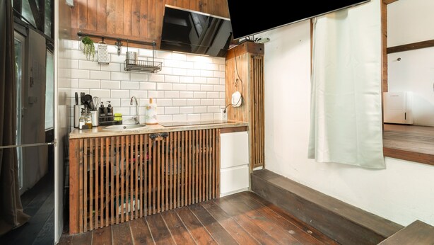 Una cocina con armarios de madera, un salpicadero de ladrillo blanco, un refrigerador de acero inoxidable y una encimera de madera.