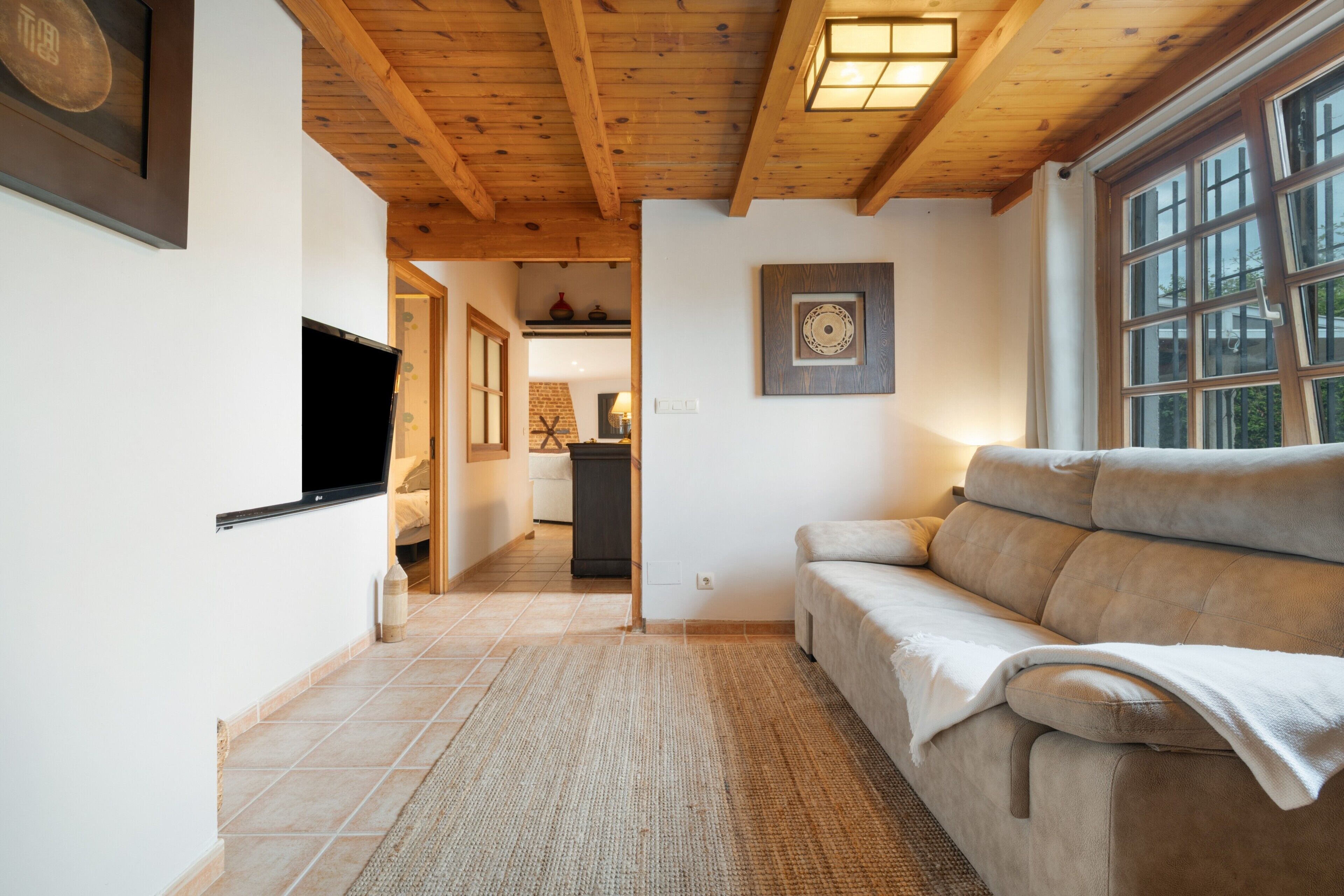 A living room with a sofa, a TV, a wooden ceiling, and a window.