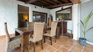 A dining area with a wooden table and woven chairs, a tiled floor, and a ceiling with exposed beams. - Acogedor chalet rústico con piscinas, Wi-Fi y aire acondicionado (Peiraio)