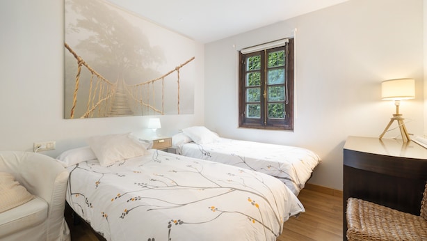 A hotel room with two beds, a desk, a chair, a window with a view, and a wall-mounted artwork. - Acogedor chalet rústico con piscinas, Wi-Fi y aire acondicionado (Peiraio)