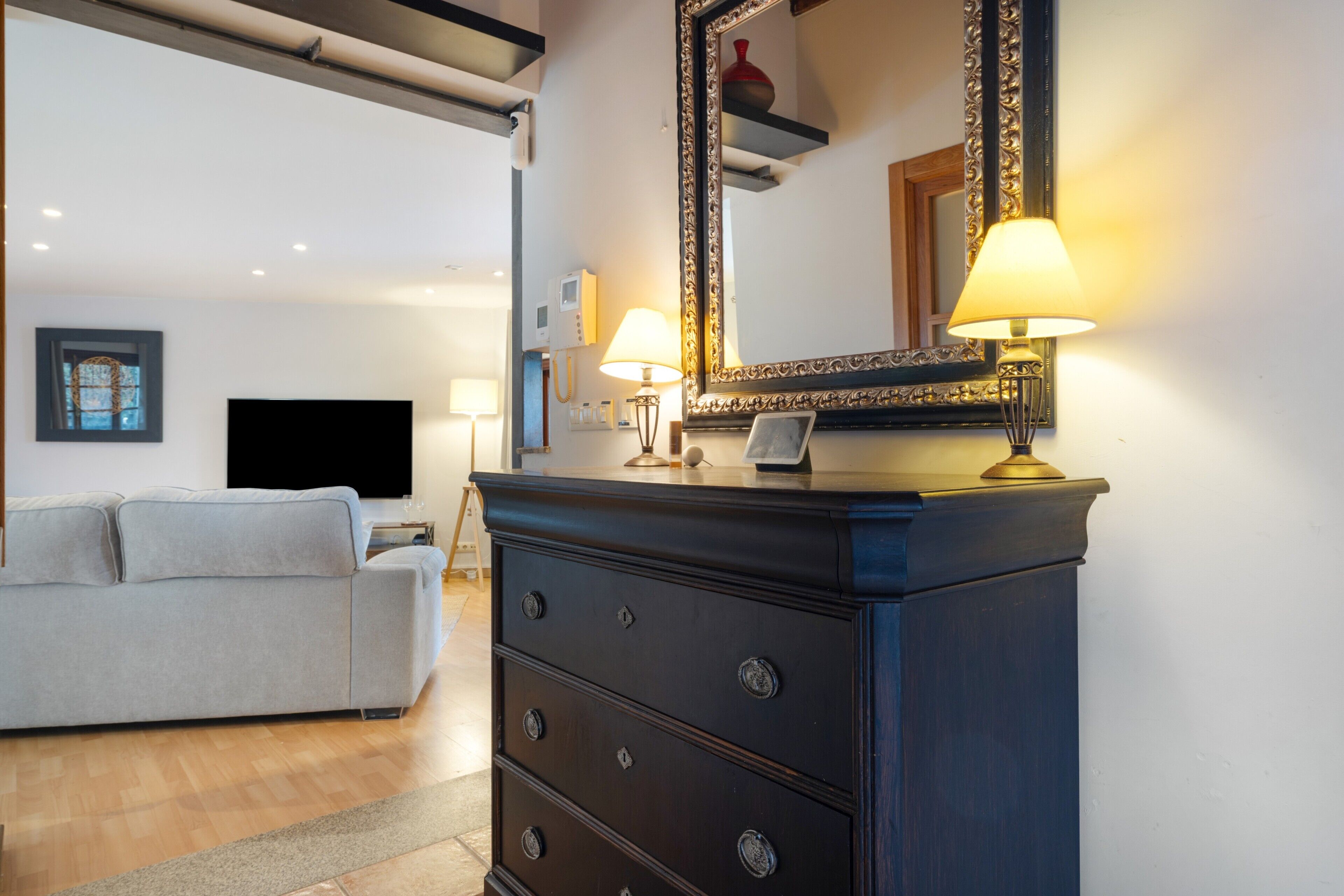Un salon moderne avec un canapé, une commode en bois foncé, un grand miroir et deux lampes fixées au mur.