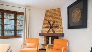 A room with a brick fireplace, two orange chairs, a white throw blanket, and a framed artwork on the wall. - Acogedor chalet rústico con piscinas, Wi-Fi y aire acondicionado (Peiraio)