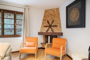 Ein Zimmer mit Kamin aus Ziegelsteinen, zwei orangefarbenen Sesseln, einer weißen Tagesdecke und einem gerahmten Kunstwerk an der Wand.