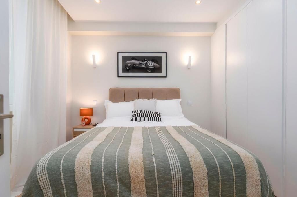 Una camera da letto ordinata con un letto, un quadro appeso al muro e una lampada da comodino.