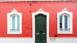 A red building with a green door and two windows with white frames.