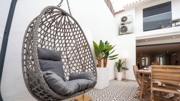 A hanging chair with cushions, a wooden table with chairs, potted plants, and a patterned floor.