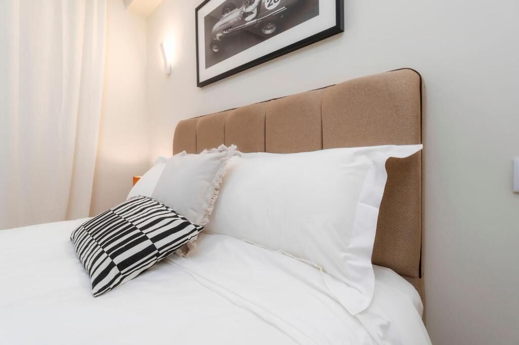Ein Bett mit weißer Bettwäsche, einem gestreiften Kopfkissen und einem Kopfteil.