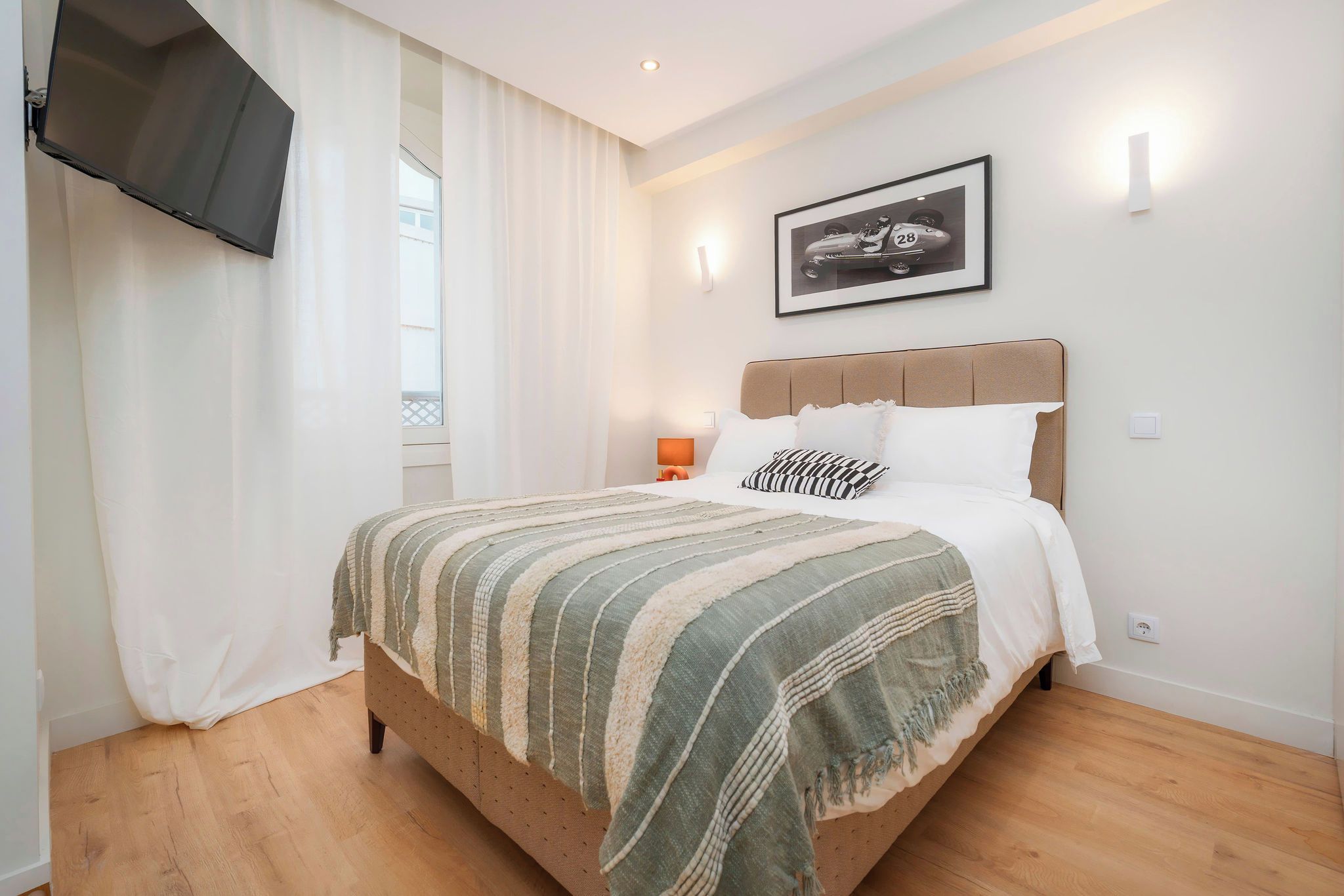 A neatly made bed with a striped blanket, a headboard, and a framed picture on the wall.