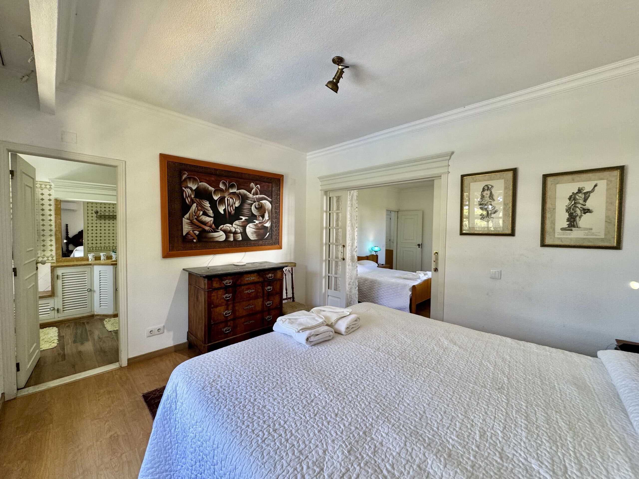 A bedroom with a large bed, a dresser, a mirror, and two framed pictures on the wall.