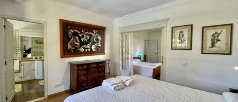 A bedroom with a large bed, a dresser, a mirror, and two framed pictures on the wall.