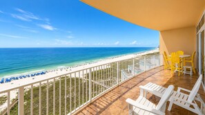 Un balcón con vista a la playa, muebles de exterior blancos y una mesa amarilla.