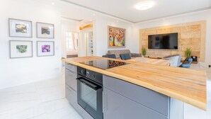 A modern kitchen with a wooden countertop, built-in oven, and a dining area with a sofa and TV. - Bel Étage Binz - Stylish Suite with a Balcony (Binz)