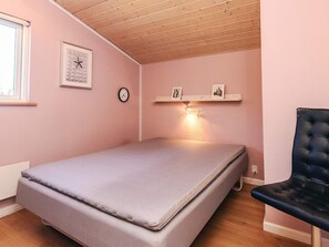 A bedroom with a single bed, a wall clock, a shelf with pictures, and a chair. - 4 Star Holiday Home in Vaeggerlose (Vaeggerlose)