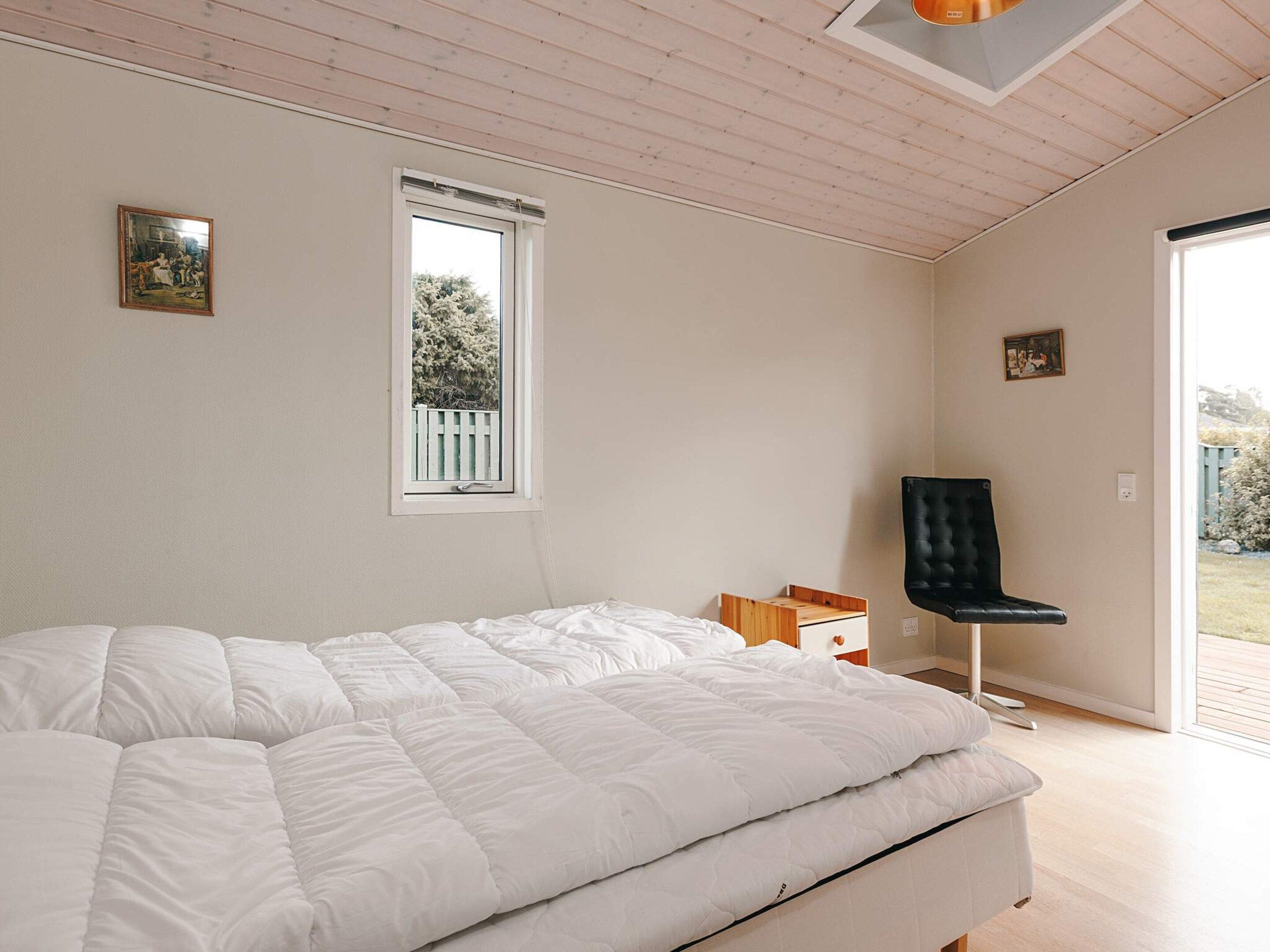 A bedroom with a large bed, a window, a chair, and a small table.