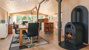 Una cucina moderna con stufa a legna integrata, zona pranzo con tavolo e sedie in legno, e vista sull'esterno tramite ampie finestre.