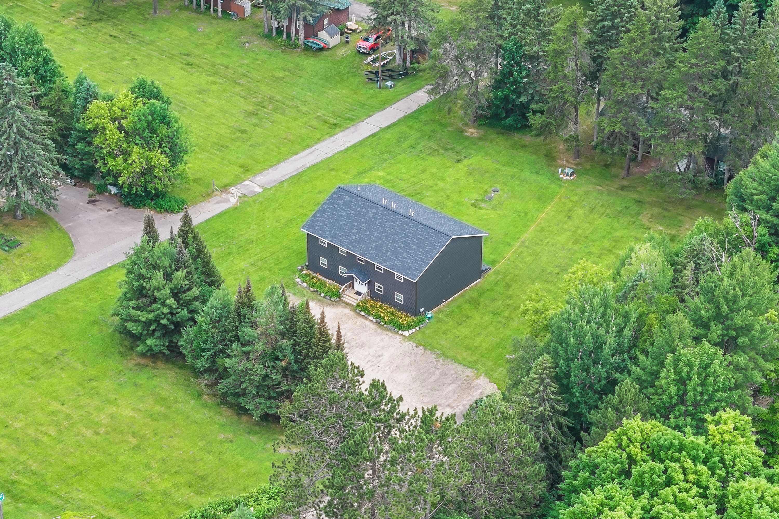 A house with a dark roof, surrounded by a well-maintained lawn and dense trees.