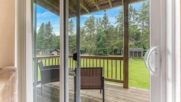 A wooden deck with a chair and a glass door leading to a grassy area with trees.