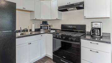 A modern kitchen with white cabinets, a black stove, a microwave, and a coffee maker.