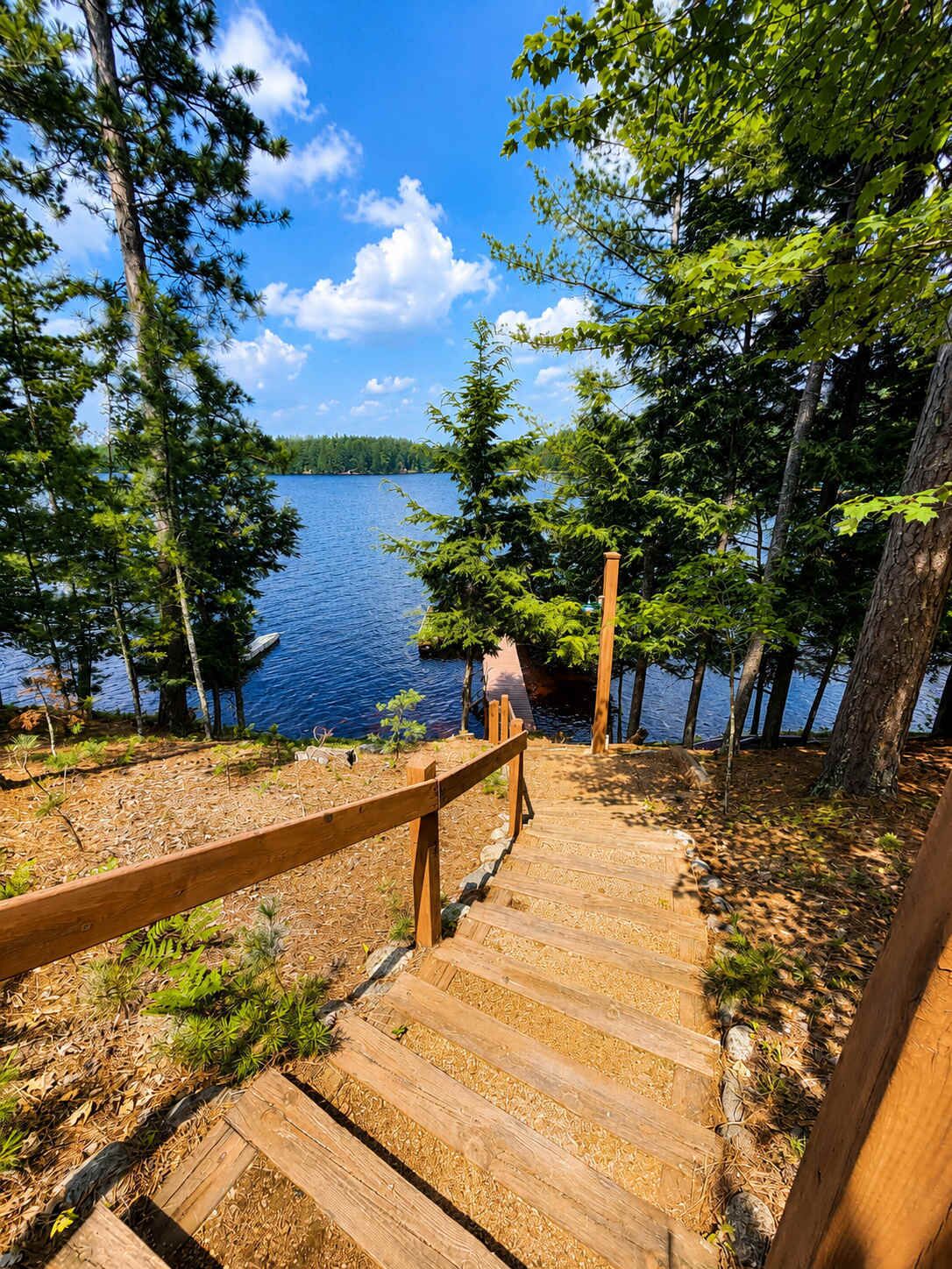 A wooden staircase leading to a dock by a lake surrounded by trees.