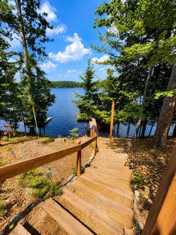A wooden staircase leading to a dock by a lake surrounded by trees. - Luxury Log Home W Sandy Frontage, Private Dock, Year-Round trails (Three Lakes)
