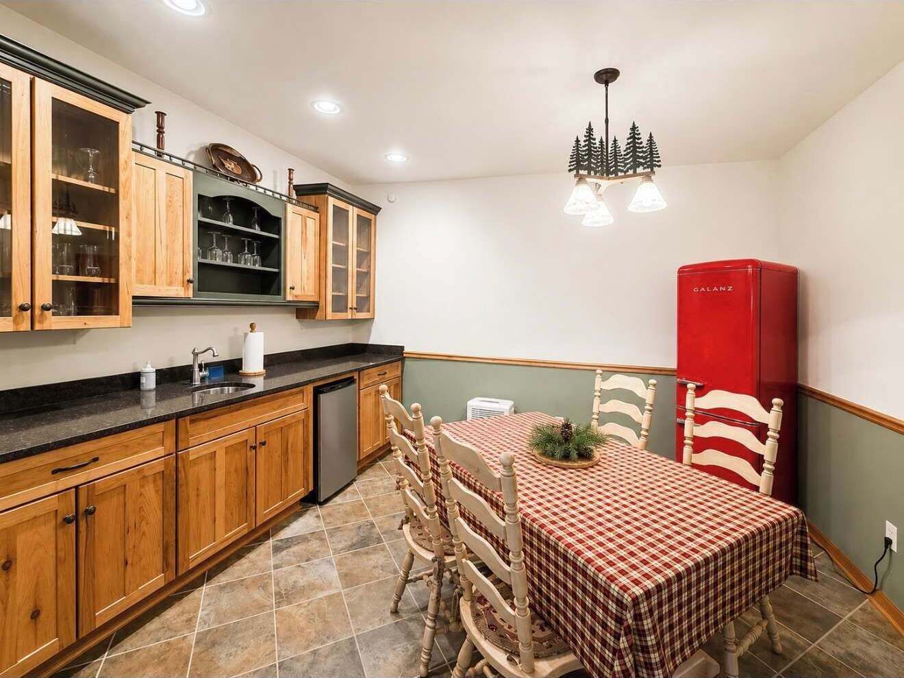 A kitchen with wooden cabinets, a dining table with chairs, and a red refrigerator.