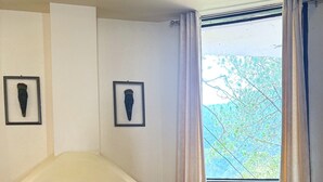 Ein Zimmer mit Holzboden, einem roten Sitzsack, einer weißen Wand mit zwei gerahmten Bildern und einem Fenster mit Vorhängen.