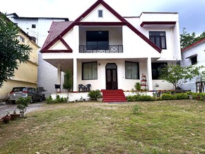 A two-story house with a red front door, a balcony, and a small garden area.