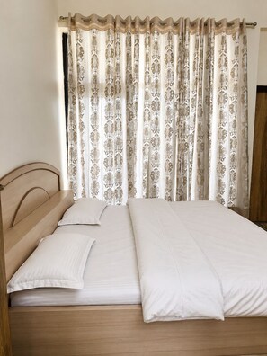 Una cama con cabecera de madera, ropa de cama blanca y cortina con estampado floral.