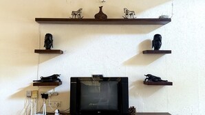 Ein Wohnzimmer mit Fernseher auf einer Holzkommode, umgeben von Regalen mit Dekoration.