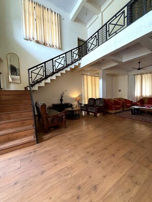 A spacious living area with a wooden staircase, a sofa set, and a dining table.