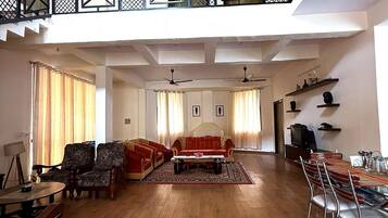 A spacious living area with a high ceiling, wooden flooring, and a balcony with a black railing.