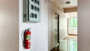 Um corredor com alarme de incêndio e painel elétrico, uma porta e uma janela no fim.