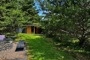 Una petita cabana de fusta amb una porta de vidre, envoltada d'arbres densos i un jardí ben cuidat.