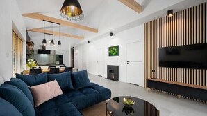 Ein modernes Wohnzimmer mit einem Ecksofa, einem runden Couchtisch und einem Flachbildfernseher, der an einer Wand aus Holzpaneelen befestigt ist.
