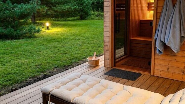 Eine Holzdielen-Terrasse mit gepolsterten Sitzgelegenheiten, ein Saunaraum mit Handtüchern und eine kleine Außenleuchte.