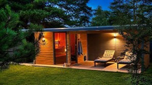 Eine moderne Holzhütte mit Glastür, zwei Loungesesseln und einer kleinen Terrasse.