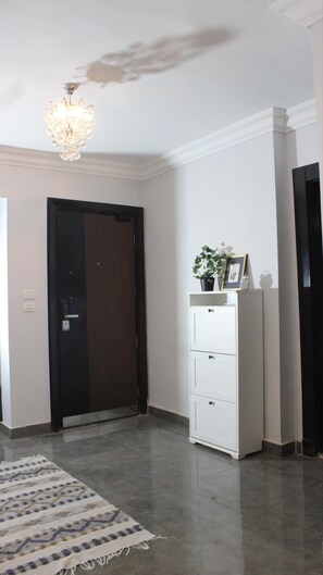 A hallway with a dark door, a white cabinet with drawers, a patterned rug, and a chandelier. - Cozy/Peaceful/Near Maadi/Ring Road/Gated Compound (Cairo Governorate)