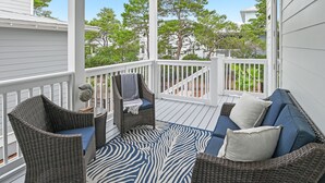 A covered porch with wicker furniture, a blue and white patterned rug, and a view of trees and houses. - 🌴 Gulfview on 30A | Resort Pool, Great Amenities & Beach Access🏖️ (Santa Rosa Beach)