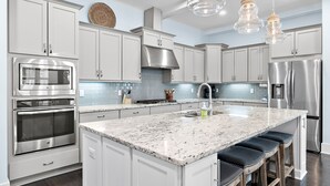A modern kitchen with white cabinets, stainless steel appliances, a granite countertop, and bar stools. - 🌴 Gulfview on 30A | Resort Pool, Great Amenities & Beach Access🏖️ (Santa Rosa Beach)