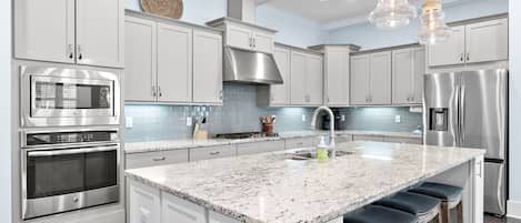 A modern kitchen with white cabinets, stainless steel appliances, a granite countertop, and bar stools.