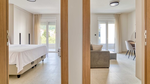 A modern bedroom with a large bed, a sofa, a dining area, and a view of the outdoors. - Mont Residence (Budva)