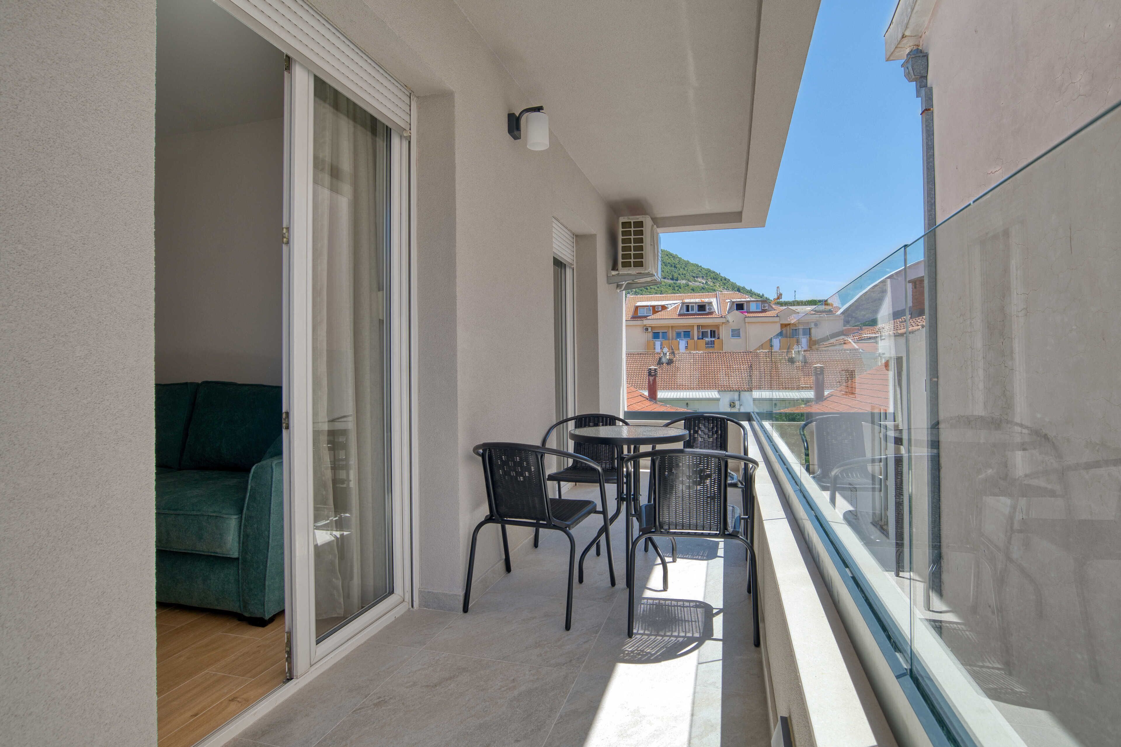 Ein Balkon mit Glastrennwand, einer Schiebetür, einem Tisch mit Stühlen und einem grünen Sofa im Inneren.