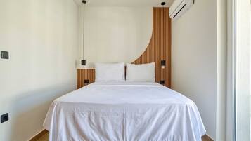 A modern hotel room with a bed, a wooden headboard, a wall-mounted air conditioner, and a window.