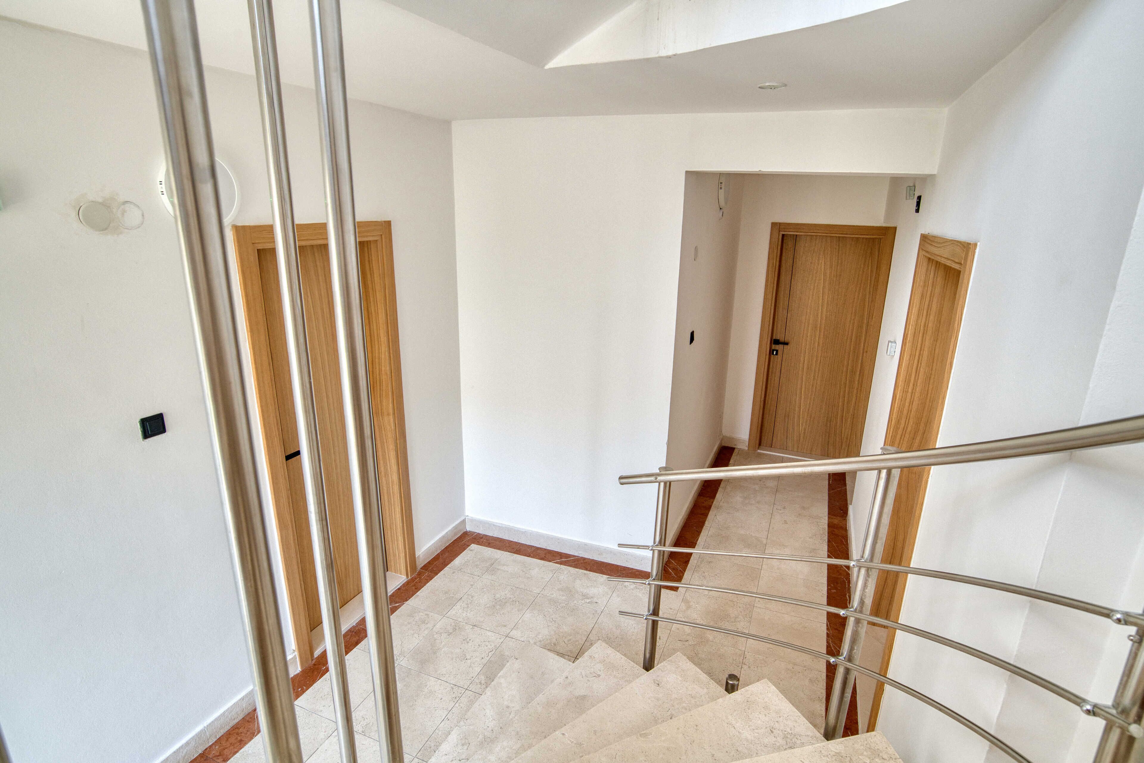 Una escalera con barandilla metálica, paredes blancas y puertas de madera.