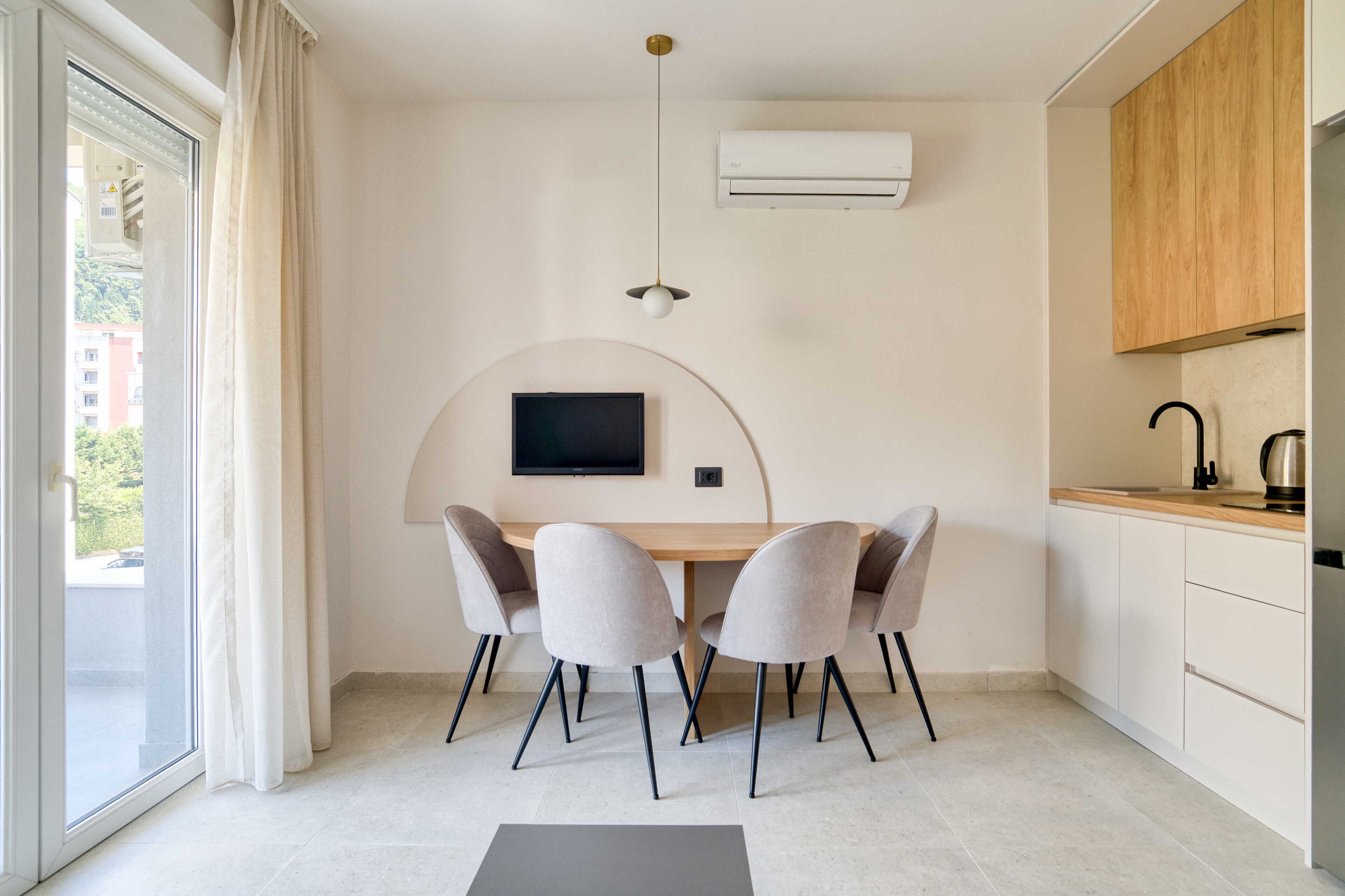 Una cocina moderna con estufa integrada, un comedor con mesa y sillas, y un amplio ventanal con cortinas.